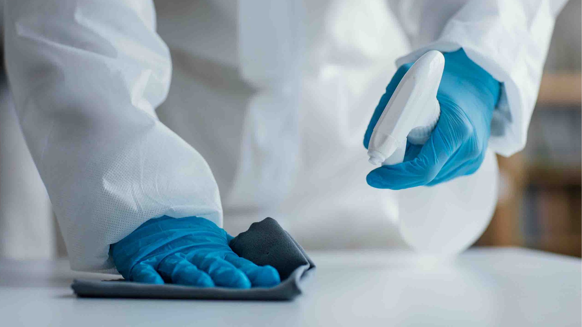 Gloved hands disinfecting a laboratory work surface